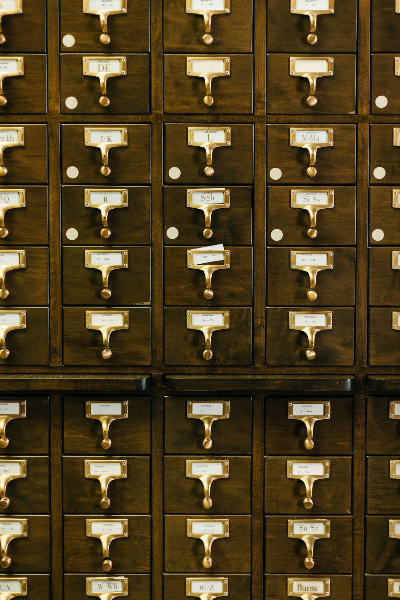 A wall of dark wood library card-catalog drawers with brass pulls and alphabetic labels.