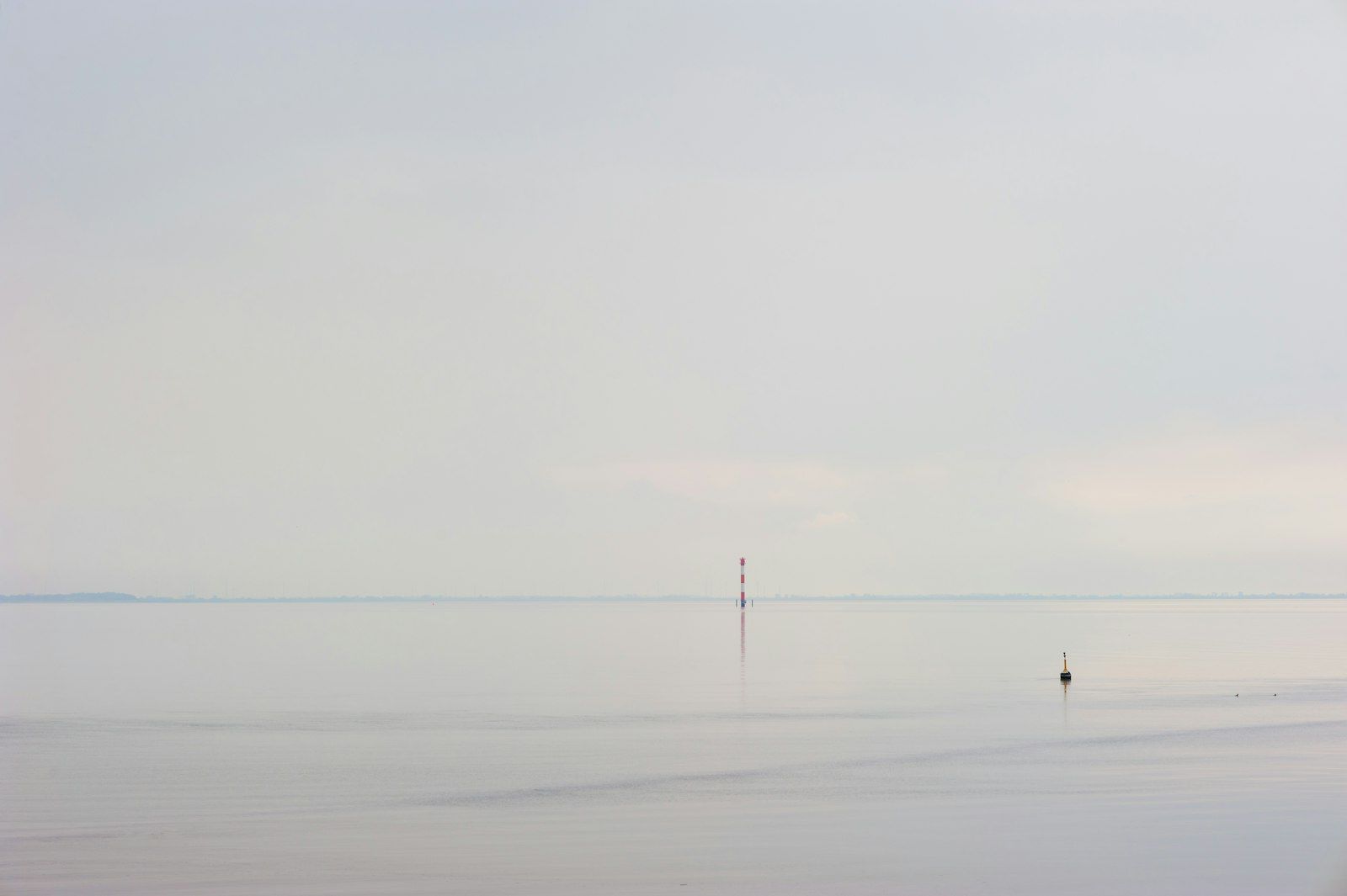 A flat, calm sea meeting an overcast sky at the horizon, almost without colour.