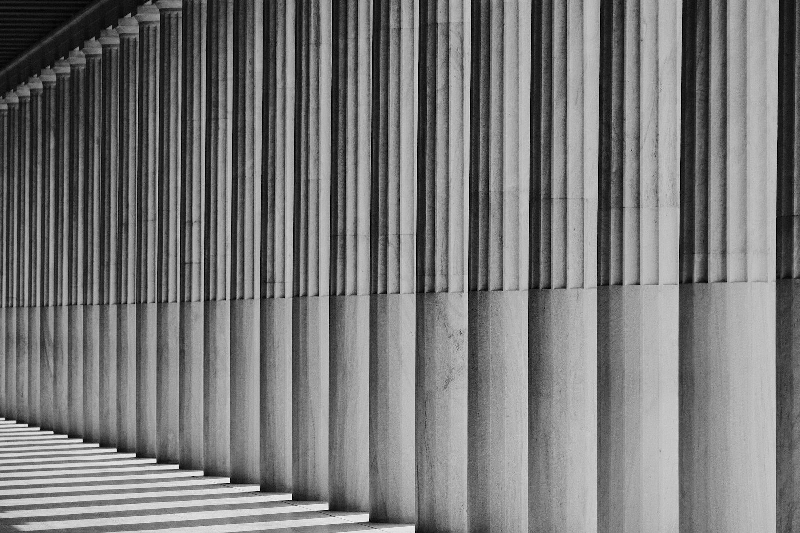 A black-and-white row of fluted stone columns receding into shadow along a colonnade.